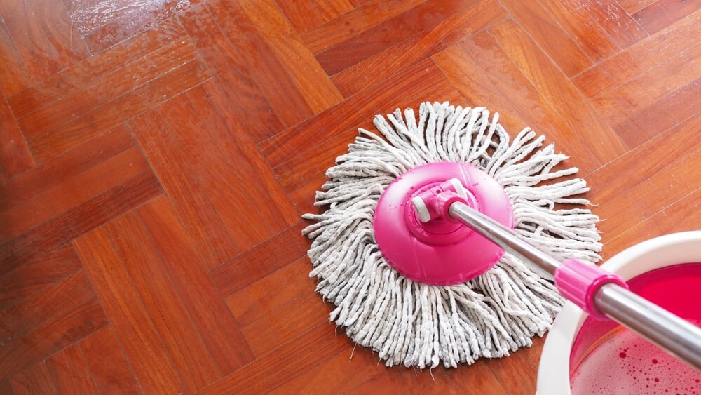A freshly refinished parquet floor being cleaned with a pink mop and bucket. The glossy surface reflects the light, showcasing the high-quality finish achieved by Mr Sander® after the sanding and refinishing process.