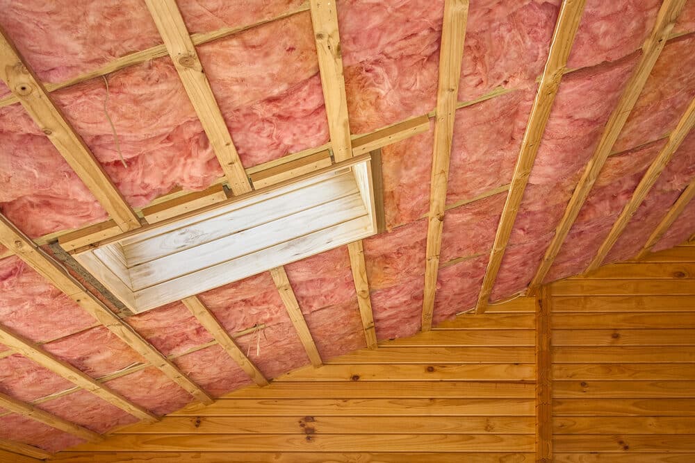 Insulated attic with pink fiberglass insulation between wooden beams.