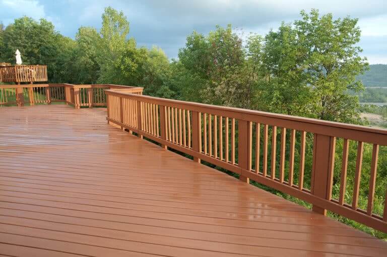 Spacious wooden deck with railing overlooking a scenic landscape after rain.