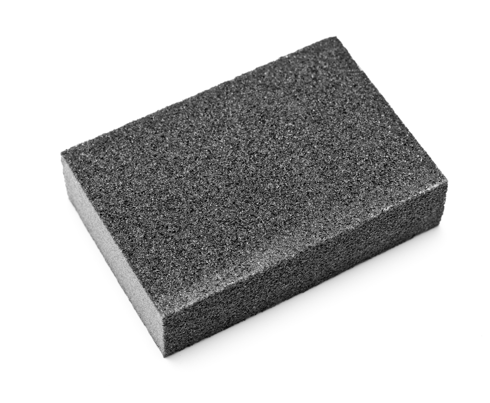A close-up image of a rectangular, black foam sponge on a white background.
