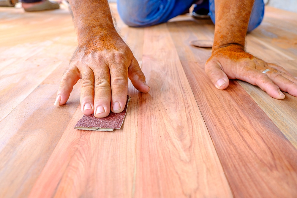 Close-up of a person's hands sanding a wooden plank with sandpaper.