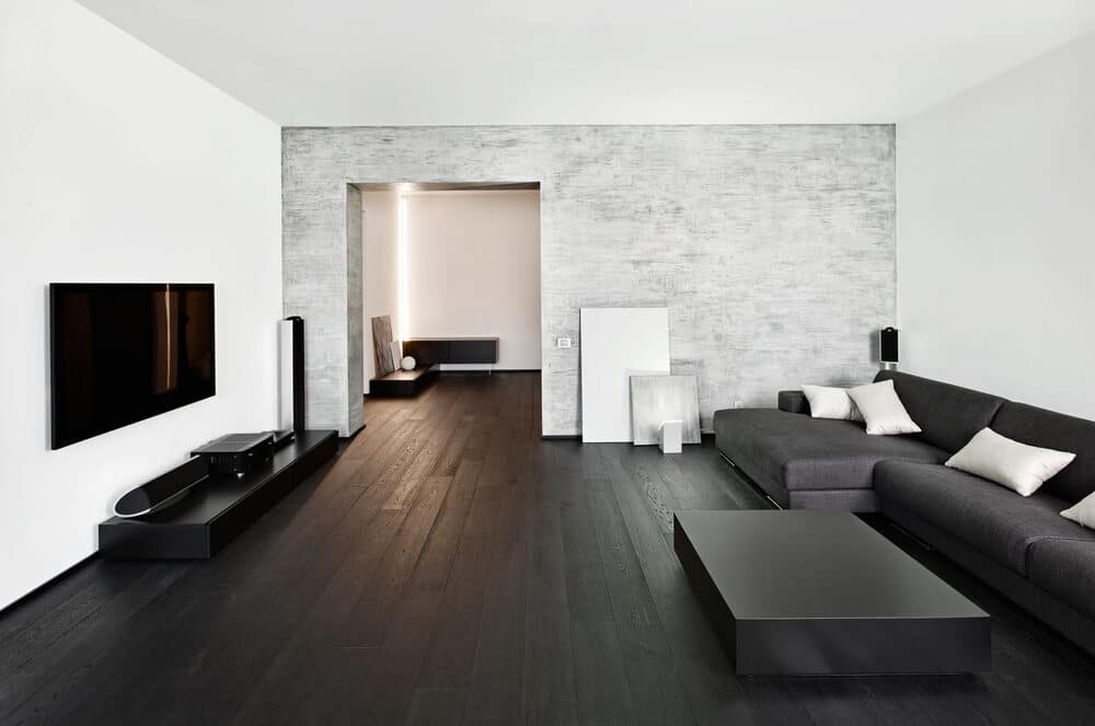 Modern minimalist living room with dark hardwood floors, a large L-shaped sofa, and a textured accent wall.