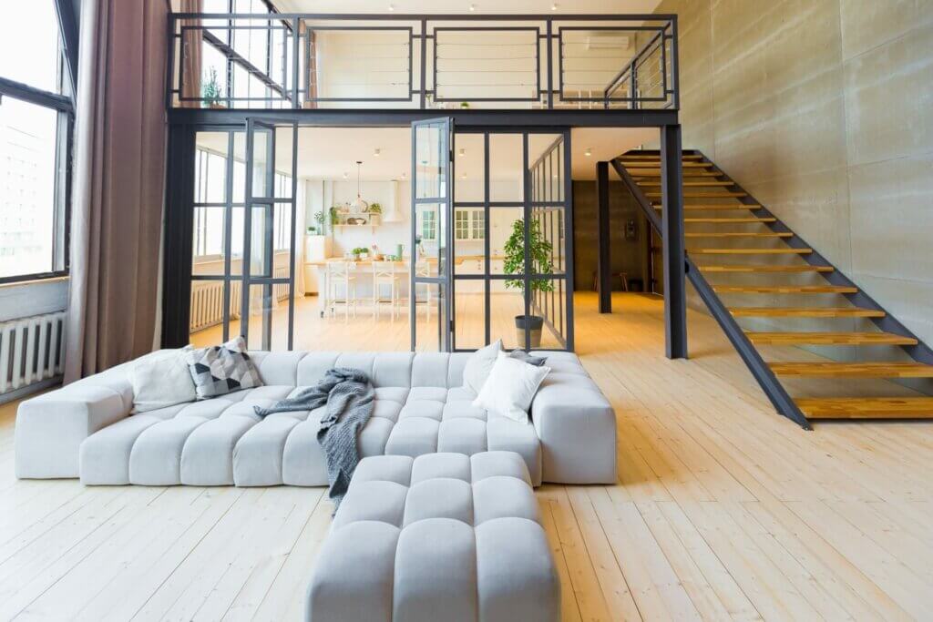 A modern living area in Dorking, UK, featuring a beautifully sanded and refinished pine hardwood floor by Mr Sander®. The spacious room includes a large sectional sofa, an open kitchen, and a stylish staircase leading to an upper loft.