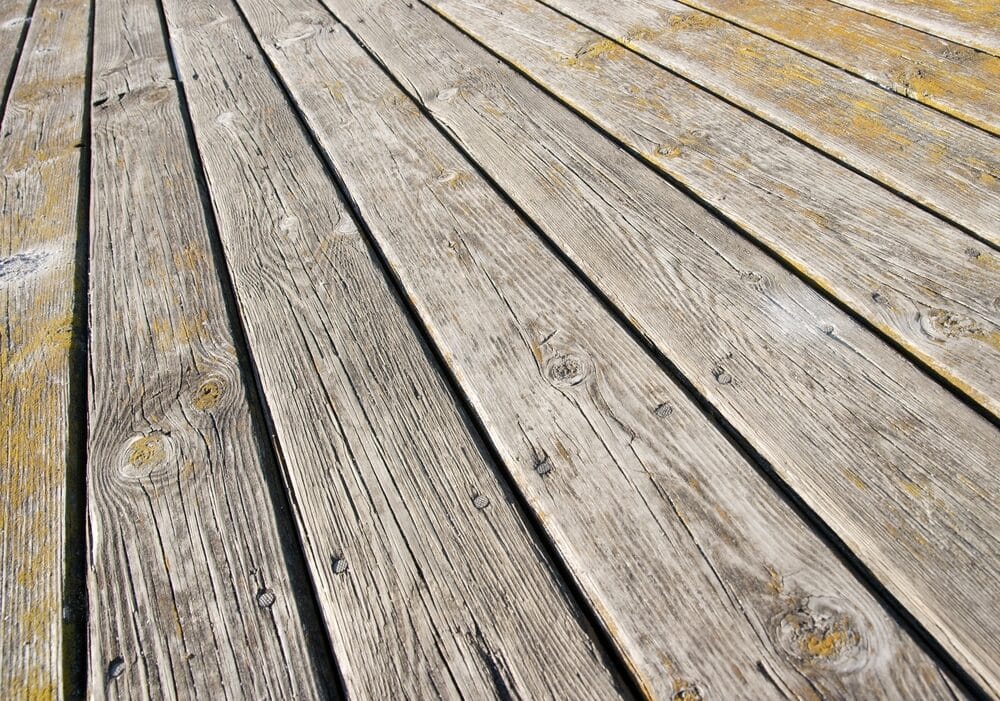 Diagonal perspective of weathered wooden planks on an outdoor deck showing signs of aging and exposure.