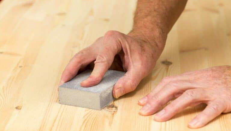Hands sanding a wooden surface with a sanding block."