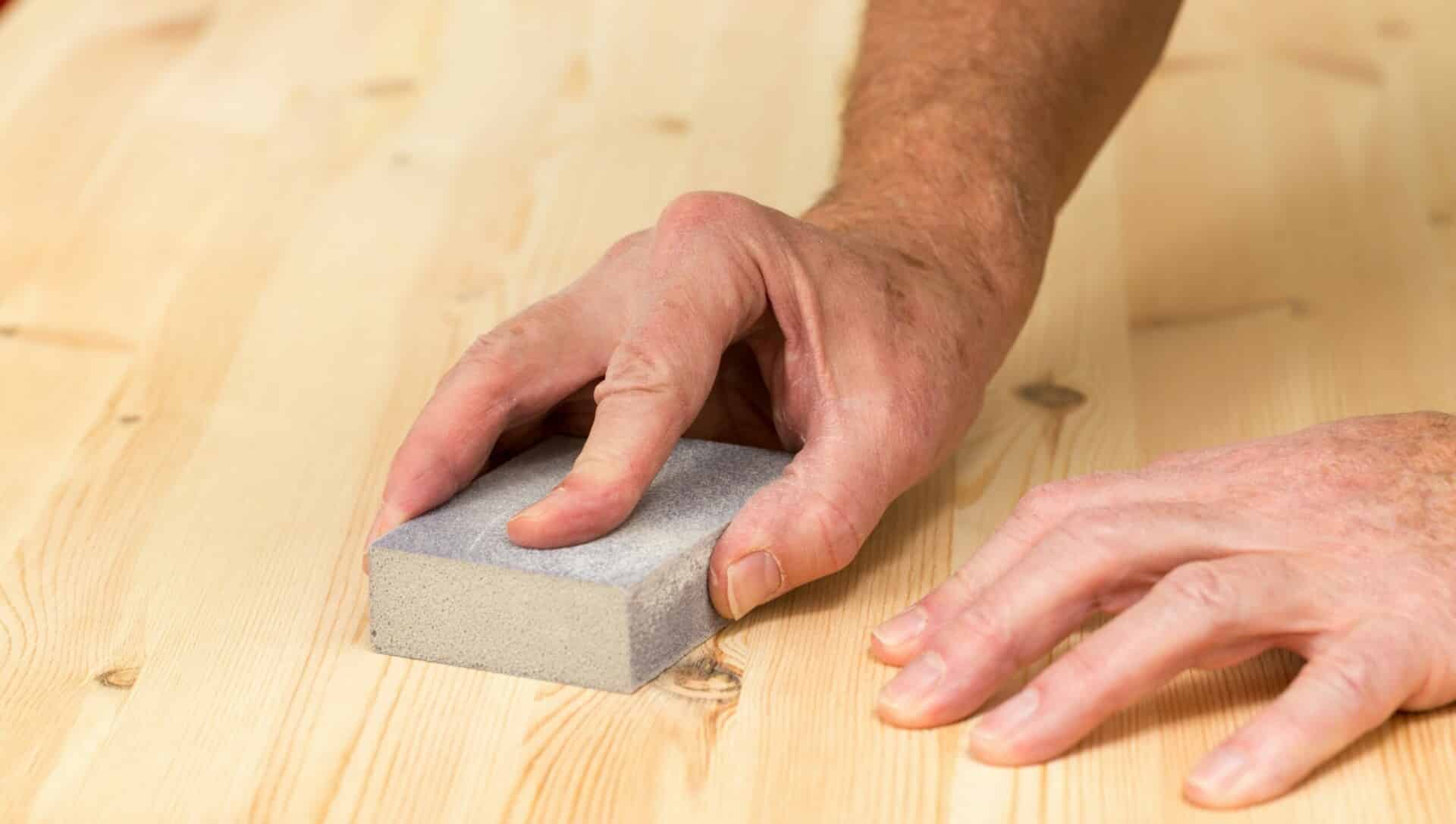 Hands sanding a wooden surface with a sanding block.