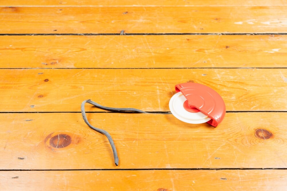 A bright orange wooden floor with visible cracks and a gap filler tool placed on it, showing the floor preparation process for sanding and refinishing.