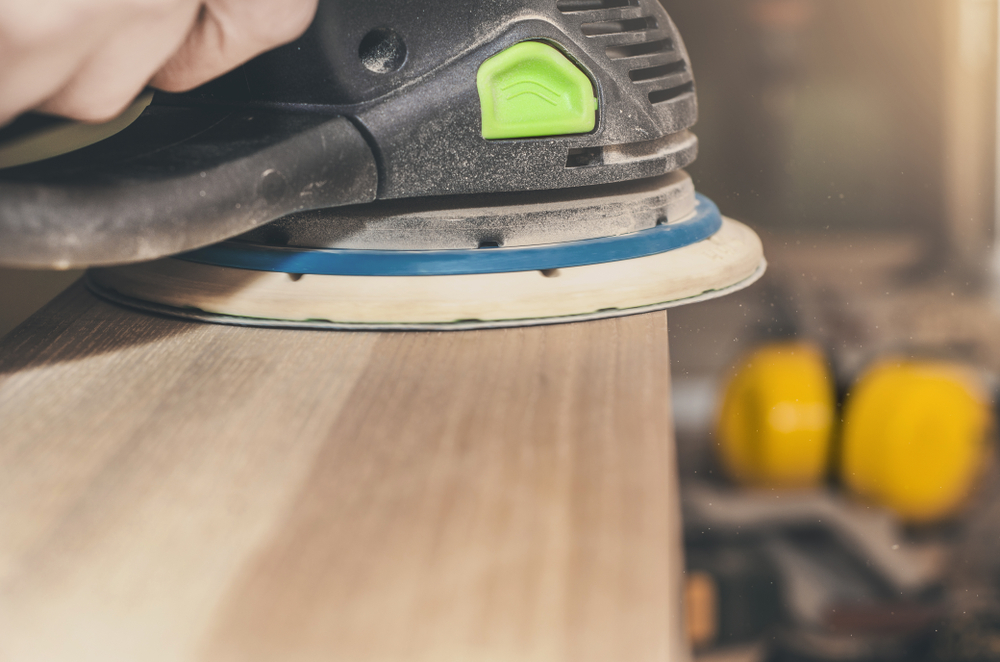 Close-up of a hand guiding an orbital sander over a wooden surface.