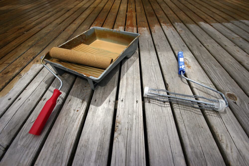 Paint tray with roller and a caulk gun on an old wooden deck.