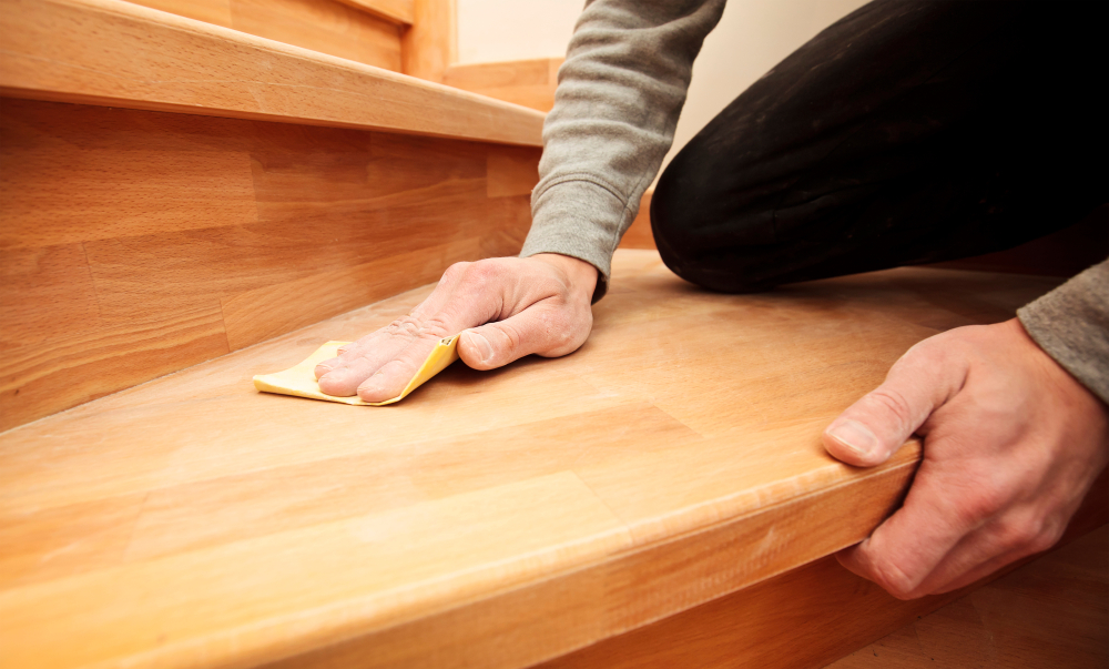 Close-up of hands sanding a wooden stair tread.