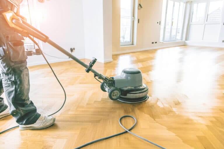 A worker operating a floor buffing machine on a parquet floor