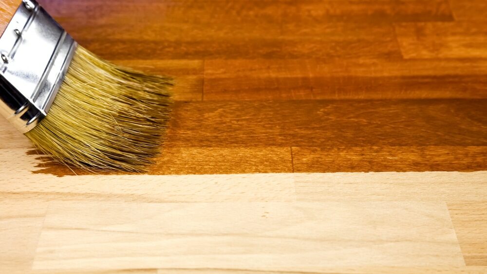 Applying a stain to a wooden surface with a paintbrush.