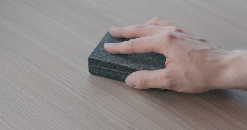 Hand pressing a black sanding block against a laminate surface.