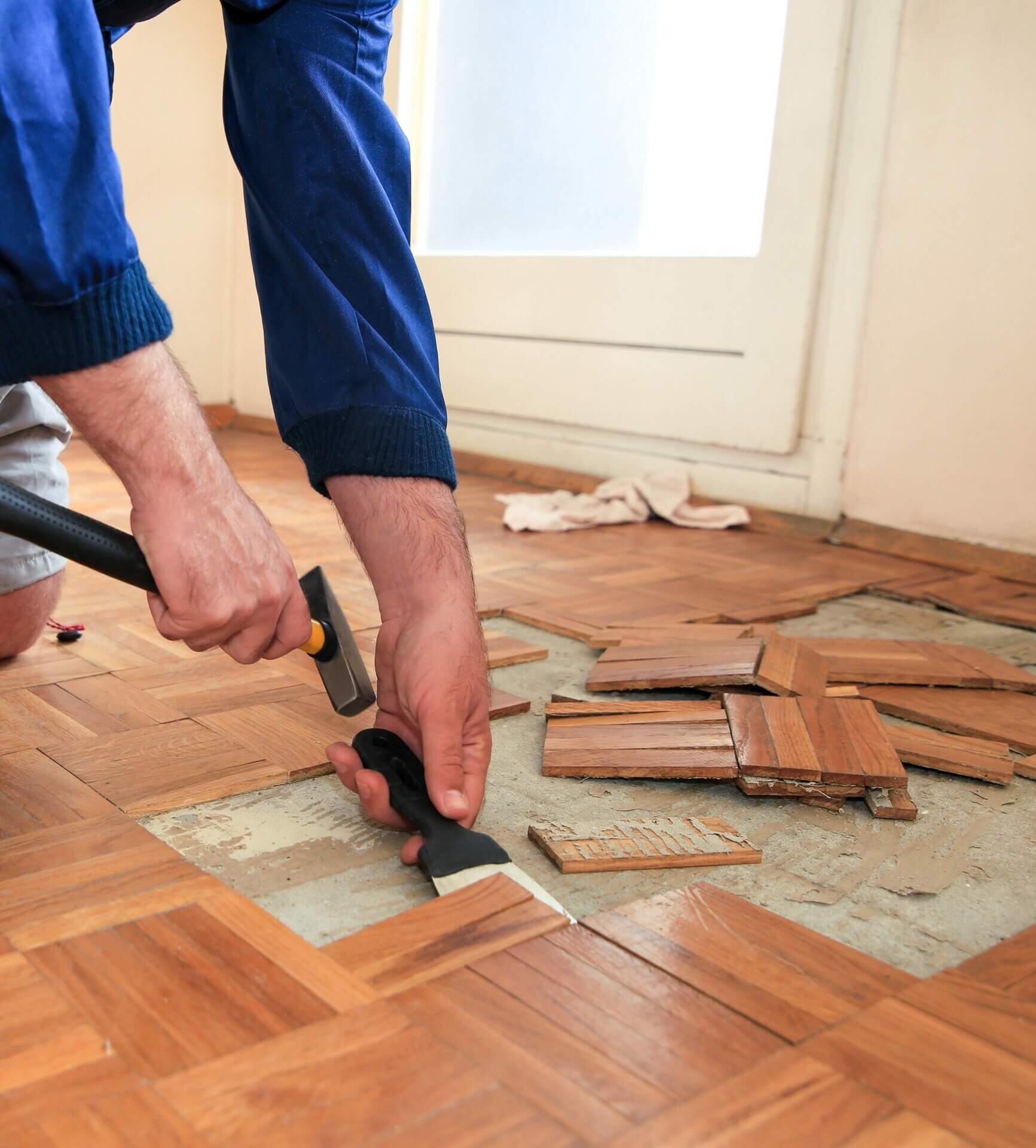 Image of a person from Mr Sander® repairing a 5 Finger parquet floor. The person is carefully removing damaged parquet tiles with tools laid beside them, showcasing the meticulous process of floor restoration
