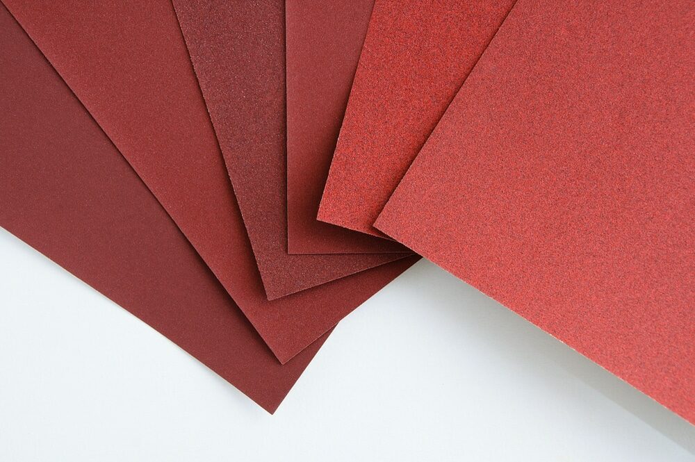 Several sheets of red and brown sandpaper fanned out on a white surface.