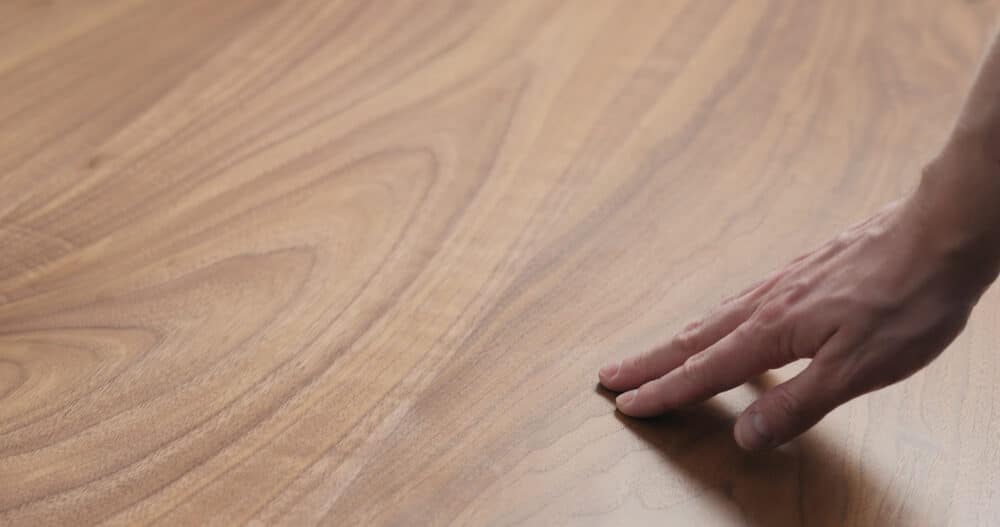 A person's hand gently touching a smooth walnut wood surface.
