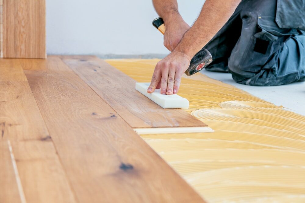 Worker applying adhesive to subfloor before laying down hardwood planks.