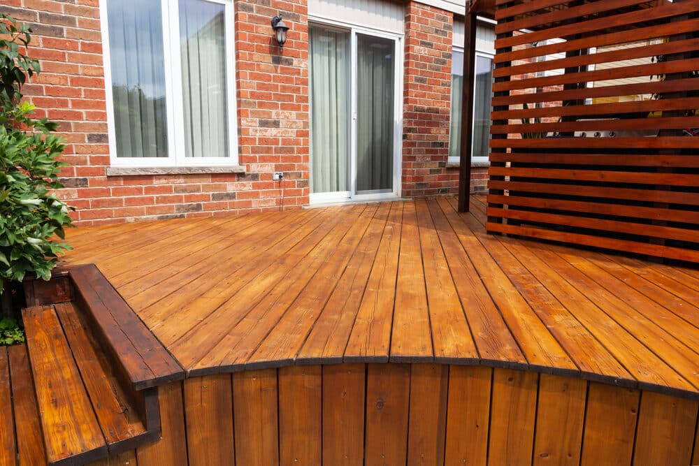 Newly stained wooden deck with a built-in bench next to a brick house