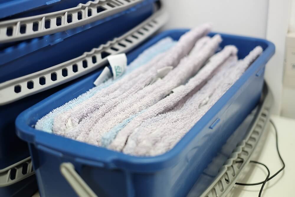 A close-up of a blue plastic bin filled with folded microfiber cleaning cloths, ready for use on newly refinished maple hardwood floors by Mr Sander®. The cleaning supplies are neatly organized, prepared to ensure a dust-free and polished surface on the maple floors after the sanding and refinishing process.