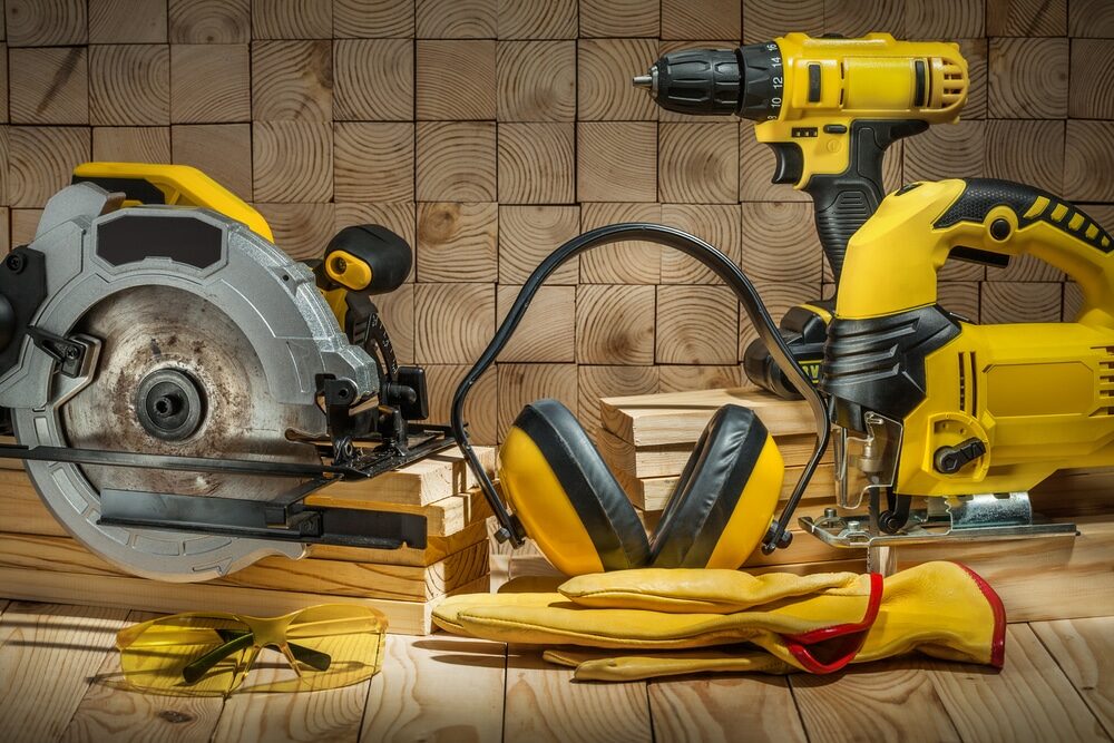 An assortment of yellow and black power tools, including a circular saw and drill, alongside safety equipment on a wooden workbench.