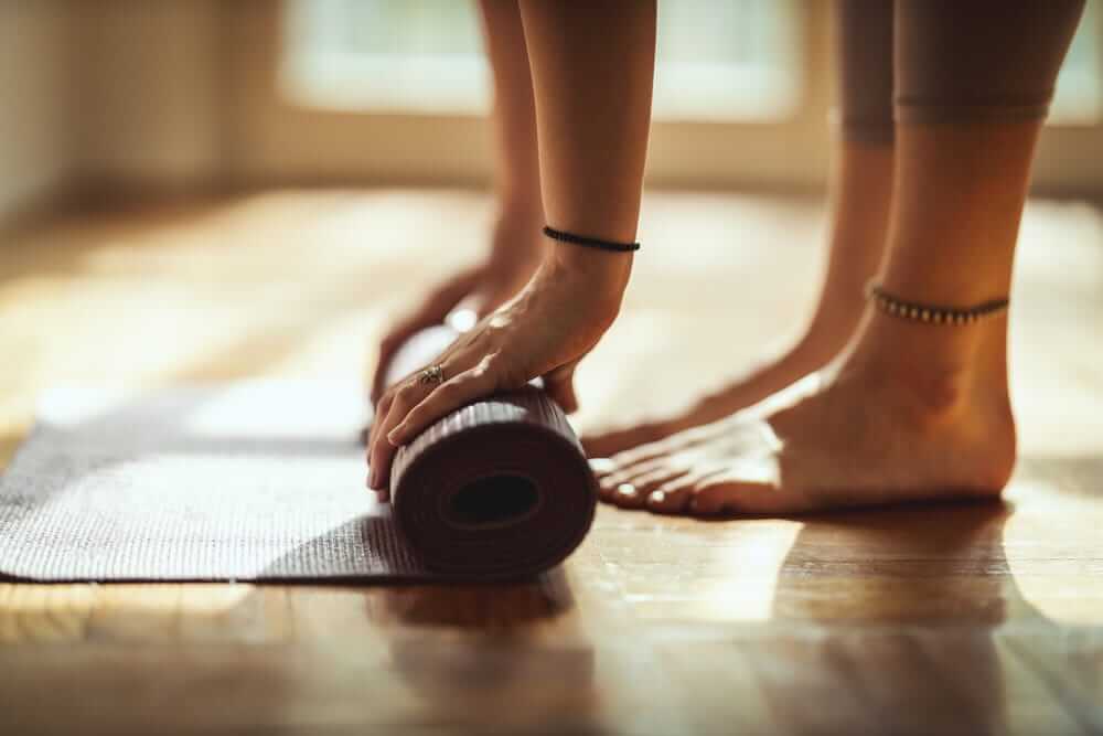 Close-up of a person rolling up a yoga mat on a beautifully refinished hardwood floor, highlighting the smooth and polished surface.