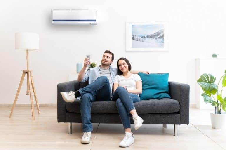 A cozy living room in a Chadwell Heath, UK home featuring a happy couple sitting on a dark grey sofa under an air conditioning unit. The room showcases beautifully refinished maple hardwood flooring, which adds a warm and inviting feel to the space. Mr Sander® provides expert floor sanding and refinishing services, ensuring that the natural beauty and durability of the maple wood are maintained.