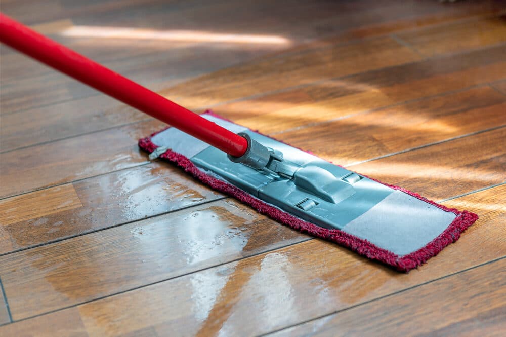 A mop with a red handle cleaning a hardwood floor.