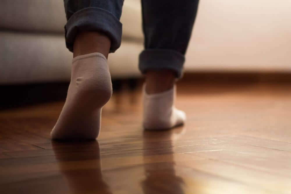 Close-up of a person's feet in socks walking on a glossy refinished wooden floor by Mr. Sander®.
