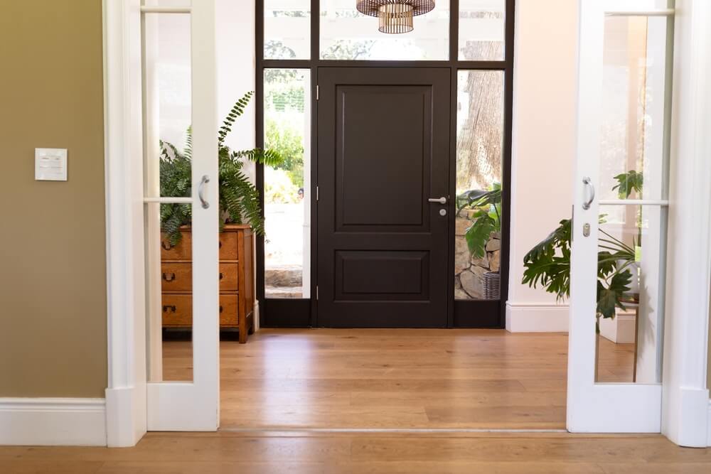 Beautifully refinished wooden floor in an elegant entryway with plants and a black front door.
