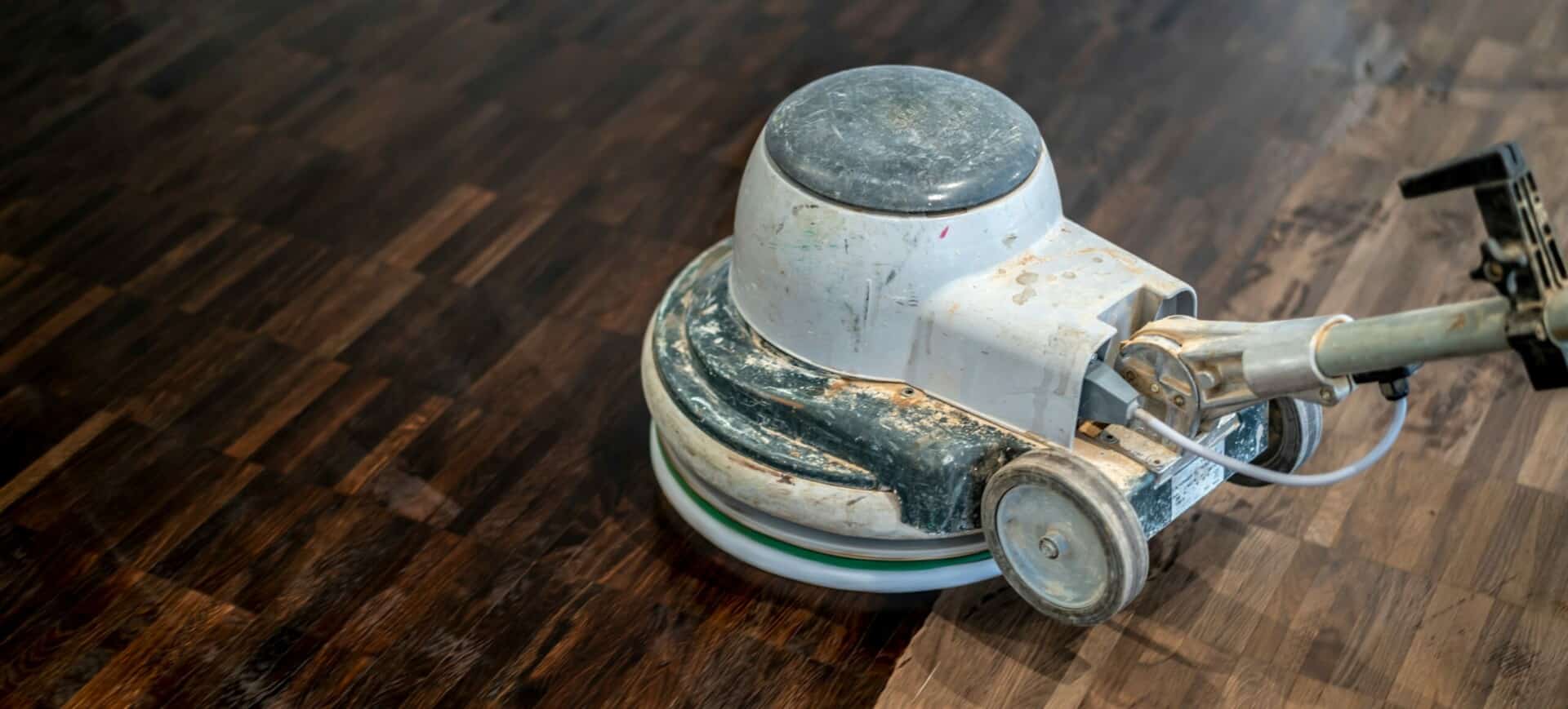 Close-up of a well-used floor buffer machine on a newly polished dark wooden floor.
