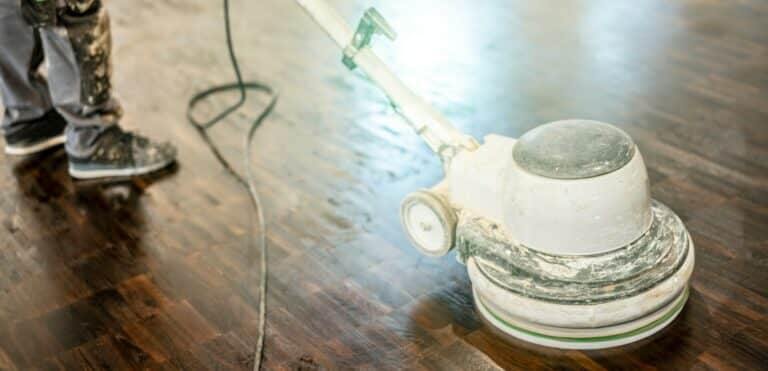 A floor buffer machine in use on a shiny wooden floor.