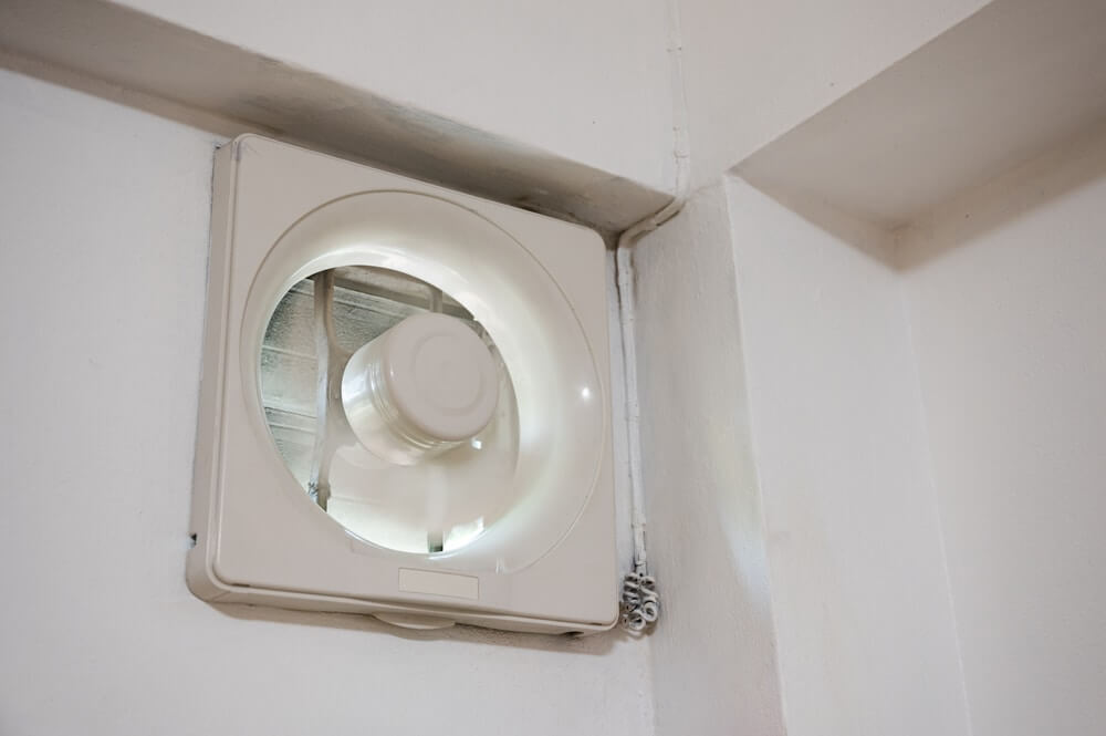 A white exhaust fan installed on a wall, used for ventilation during floor sanding and refinishing work. The fan ensures proper air circulation and minimizes dust accumulation.