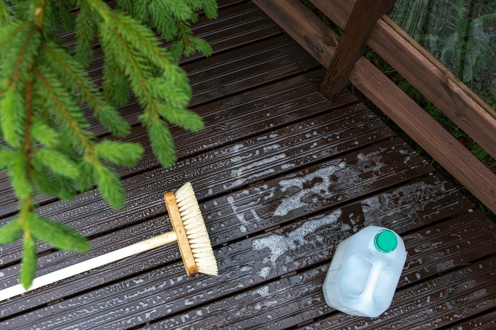 Deck cleaning with a scrub brush and a bottle of cleaning solution.