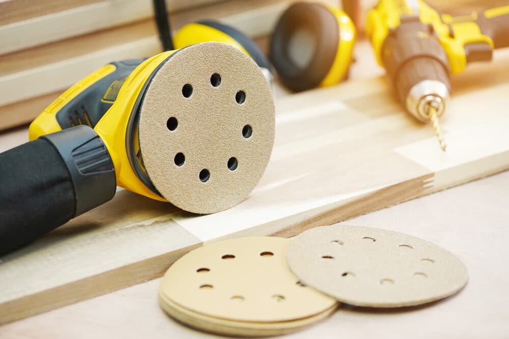 Electric sander and drill with sanding discs on a wooden workbench.