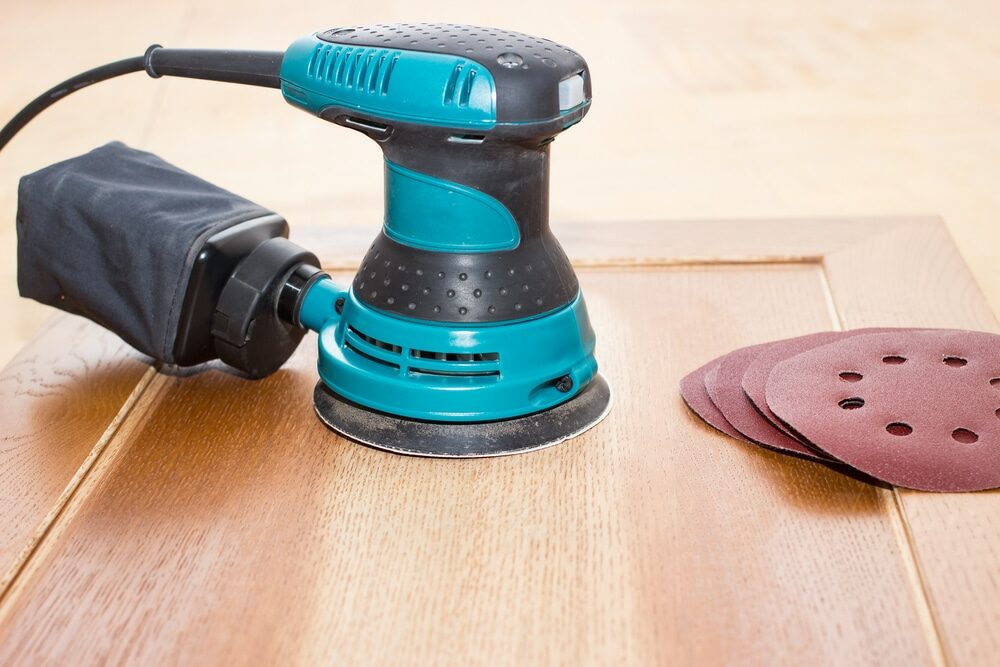 Electric orbital sander on a wooden surface with sandpaper discs.