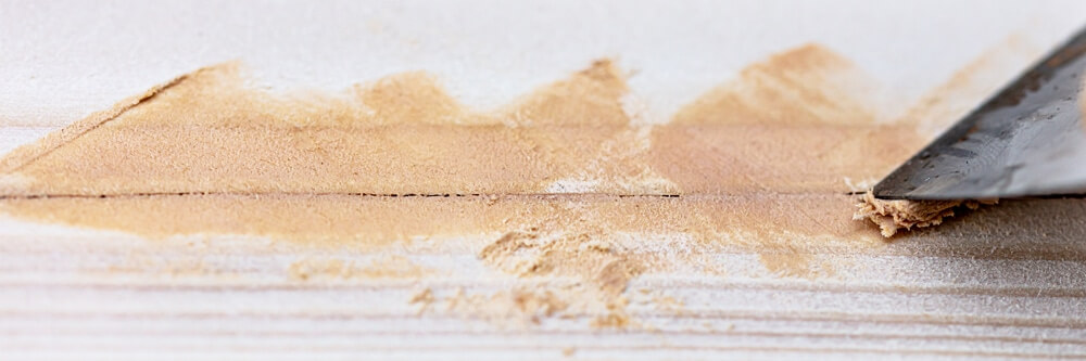 Close-up of a putty knife spreading wood filler on a wooden surface, preparing the floor for sanding and refinishing.