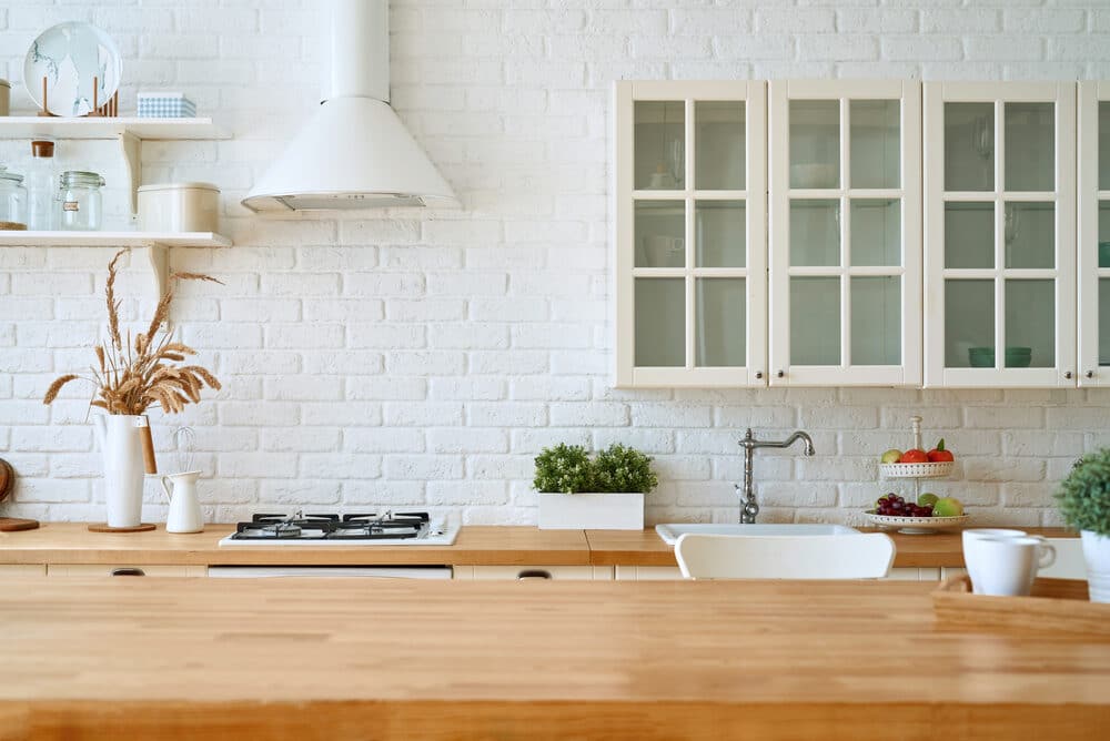 Modern kitchen interior with a white brick wall, wooden countertops, and a bowl of fresh fruit.