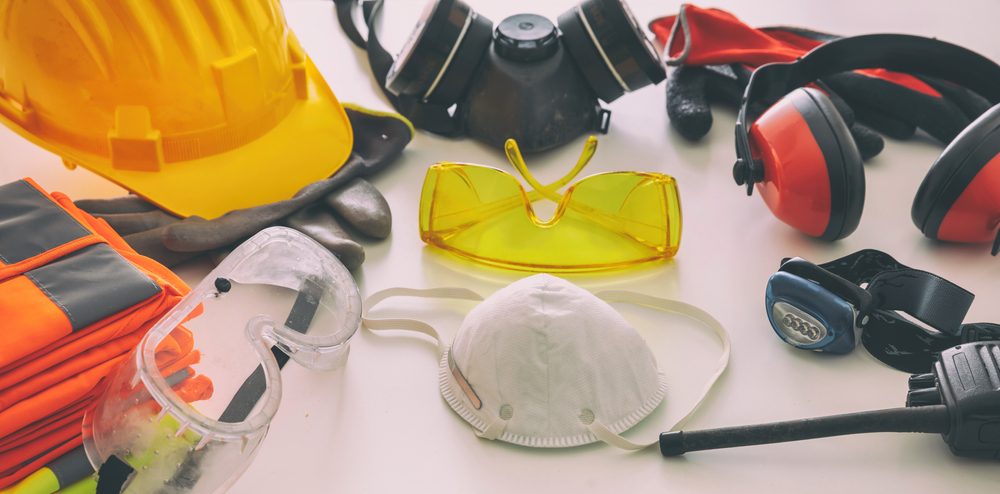  A collection of safety equipment including a yellow helmet, goggles, ear protection, a mask, gloves, and other tools on a white surface.