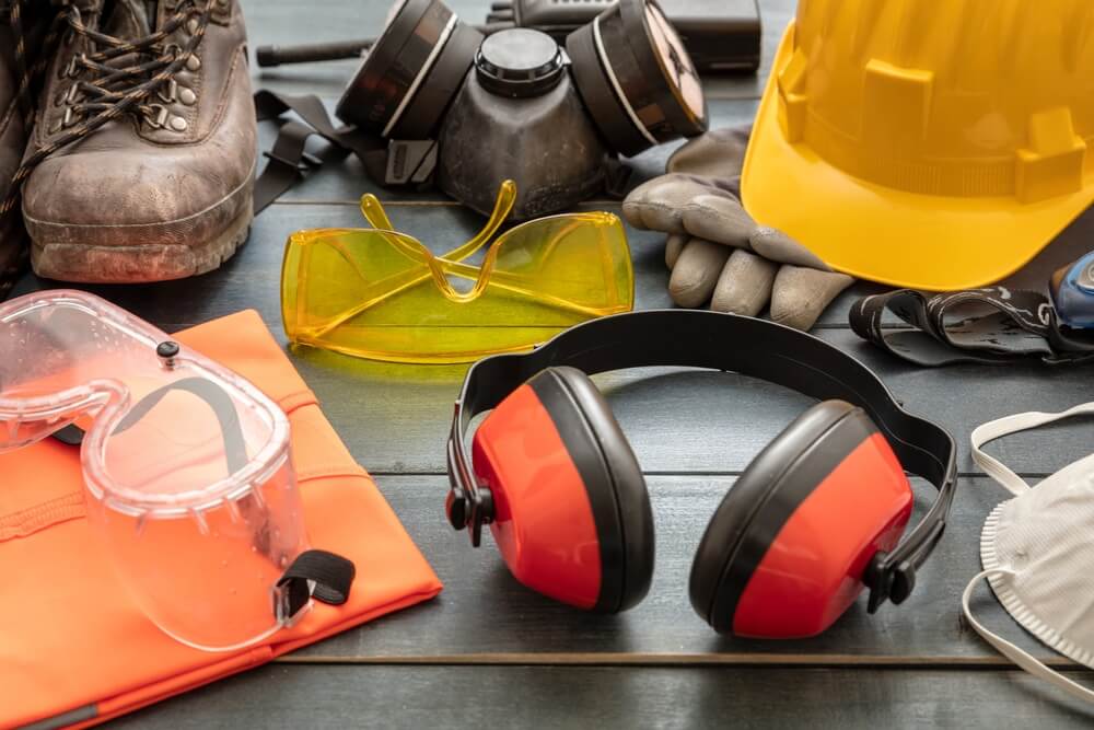 A collection of essential safety gear for floor sanding and refinishing by Mr Sander®, including a hard hat, safety goggles, ear protection, gloves, a respirator mask, and sturdy boots. The equipment ensures protection from dust, noise, and potential hazards during the sanding process.