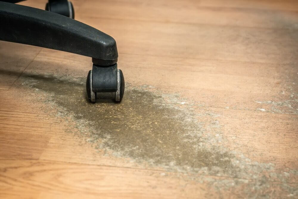 Close-up of a wooden floor with visible lacquer damage caused by chair wheels, highlighting wear and tear before Mr. Sander®'s professional office floor sanding treatment.