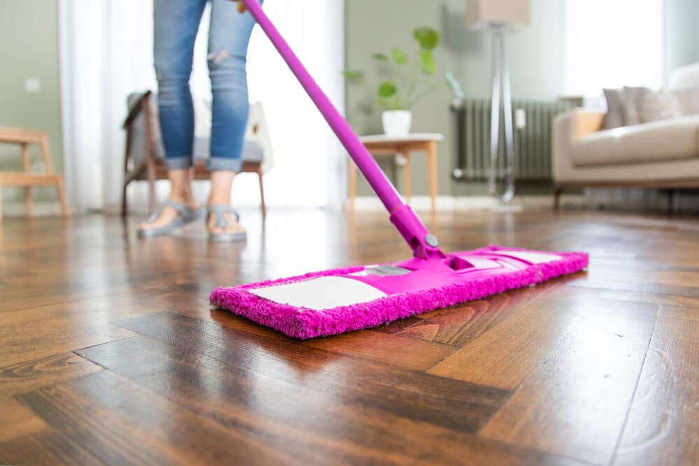 A person using a purple mop with a pink microfiber pad to clean a wooden floor