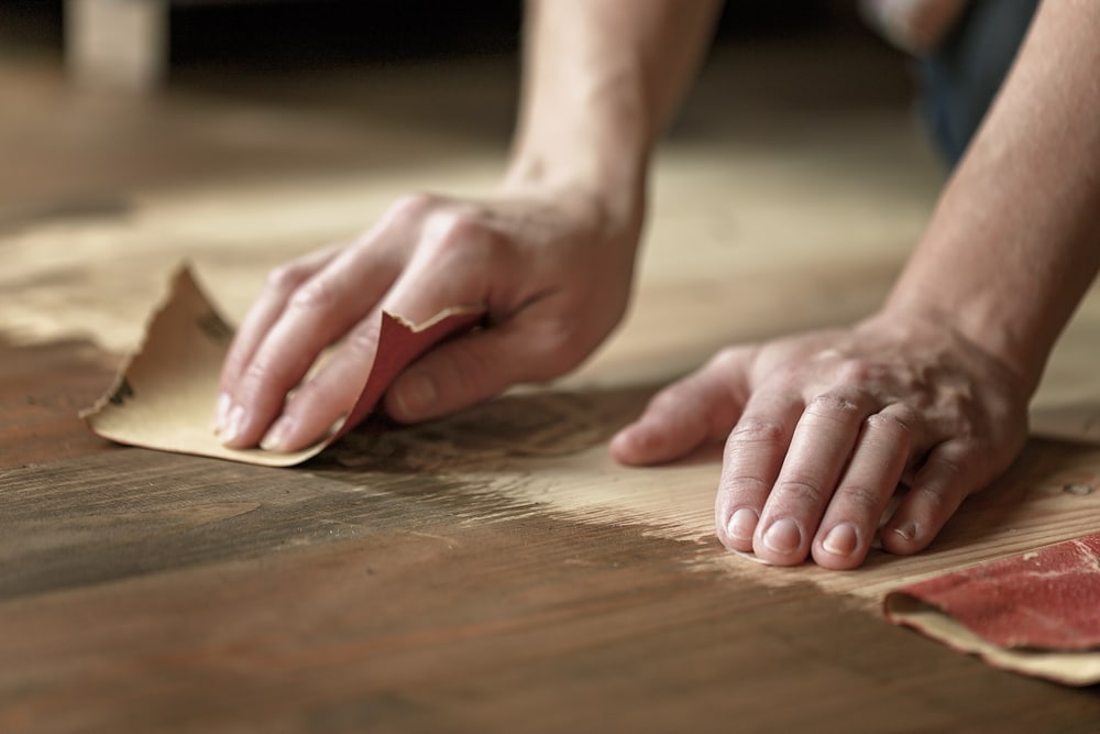 Close-up of hands sanding a wooden surface with sandpaper.