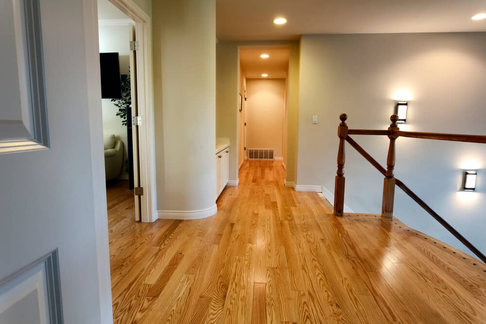 An inviting hallway featuring polished wooden floors, a staircase with wooden balustrades, and warm wall sconces.
