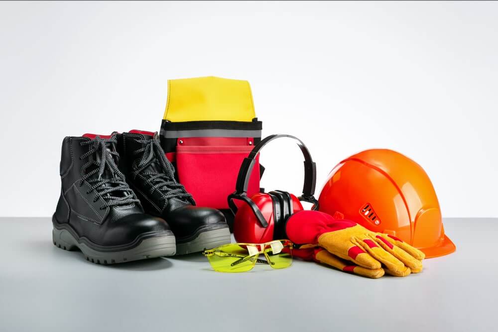 A collection of safety equipment including black work boots, a yellow and red tool pouch, red ear protection, safety glasses, red and yellow work gloves, and an orange hard hat. These items are essential for the floor sanding and refinishing work done by Mr Sander®.