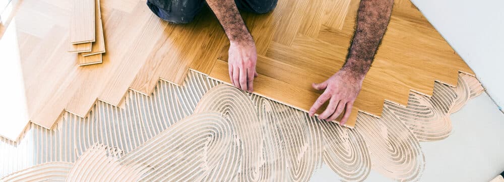 A person installing parquet flooring in a herringbone pattern.