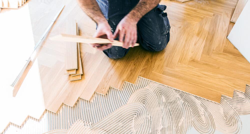  A person kneeling and installing parquet flooring in a herringbone pattern.