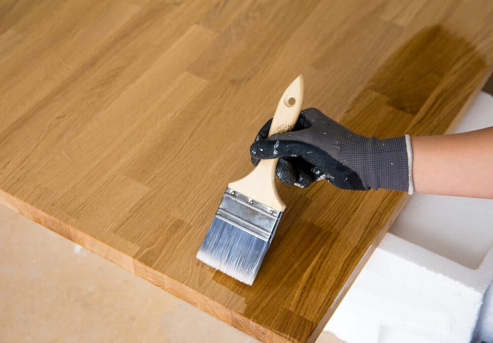 Hand applying varnish to a wooden surface with a paintbrush