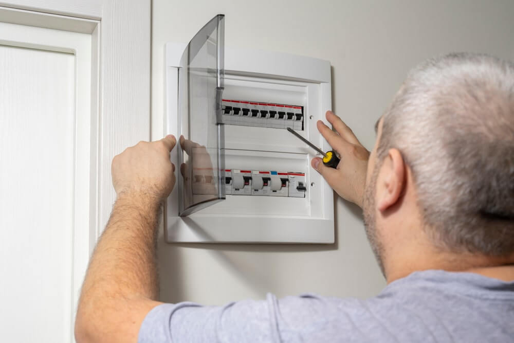  An electrician working on a residential circuit breaker panel with a screwdriver.