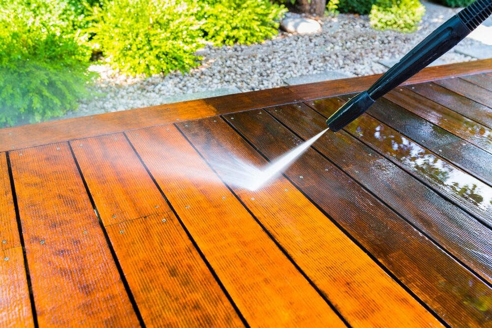 High-pressure water cleaning a stained wooden deck.