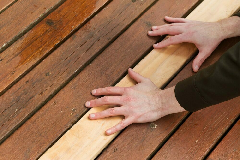 Hands placing a new wooden plank into a gap on a deck.